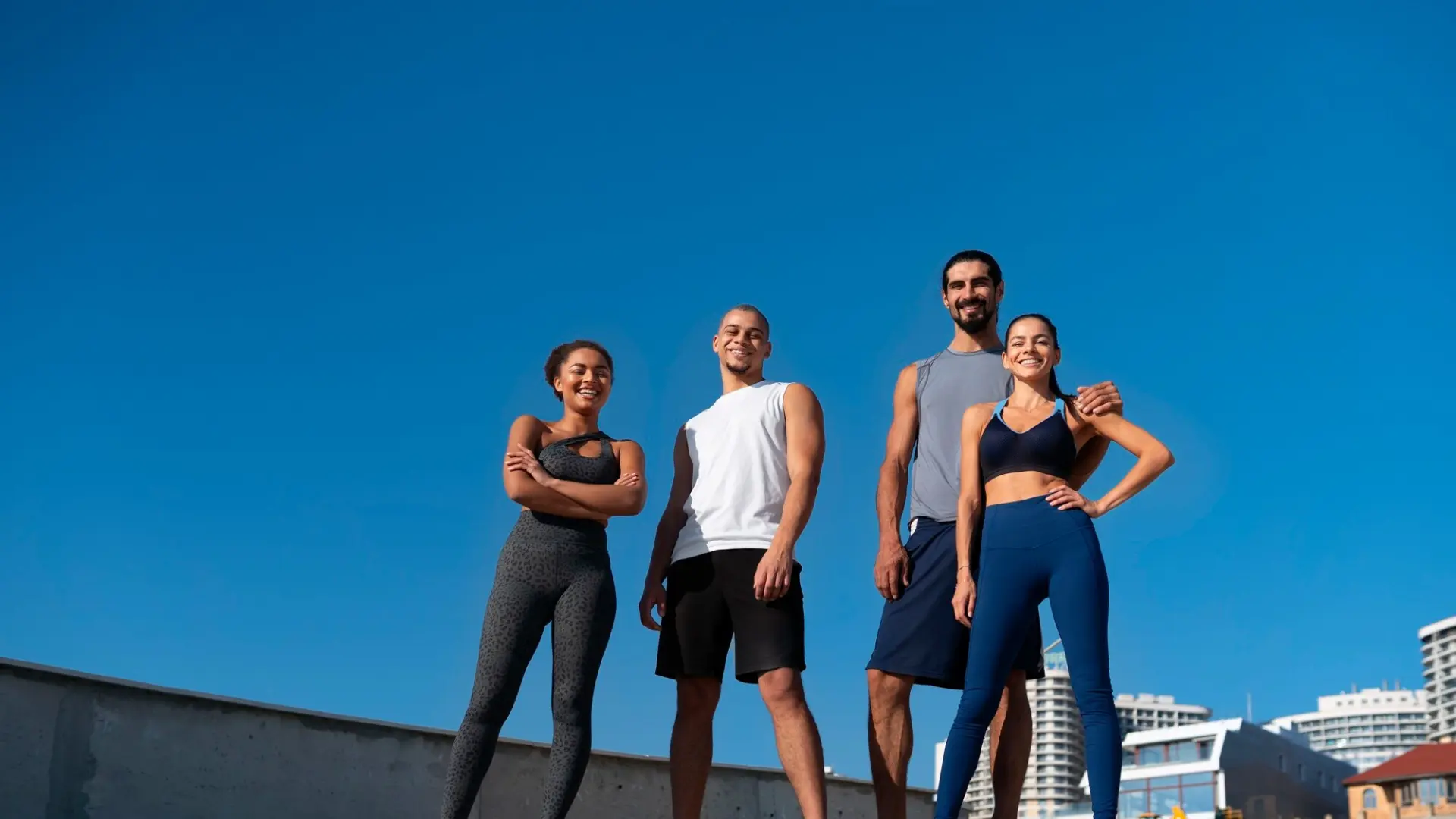 Four people in sportswear smiling outdoors under a clear blue sky.