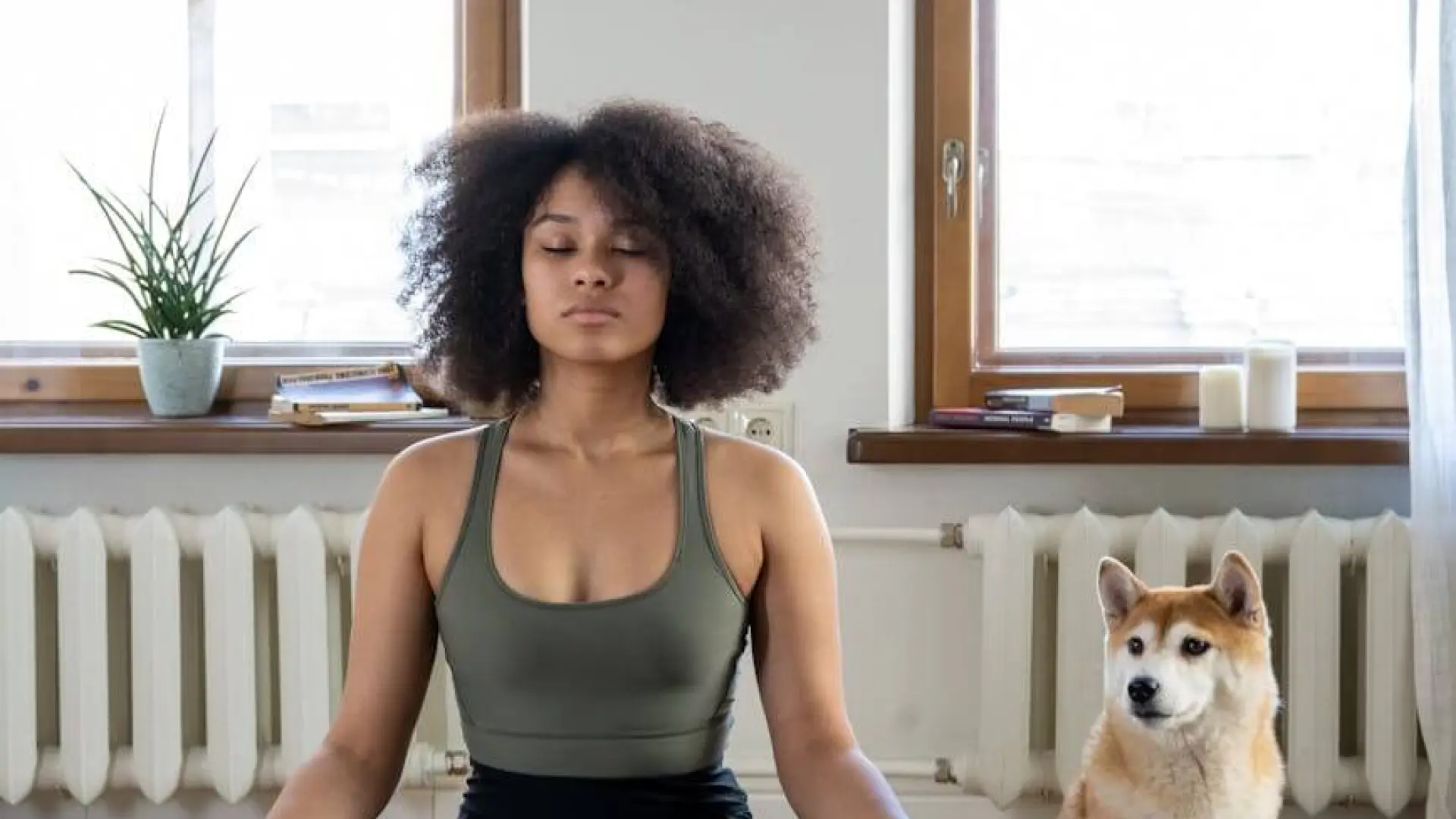 Woman meditating on yoga mat with dog beside her.