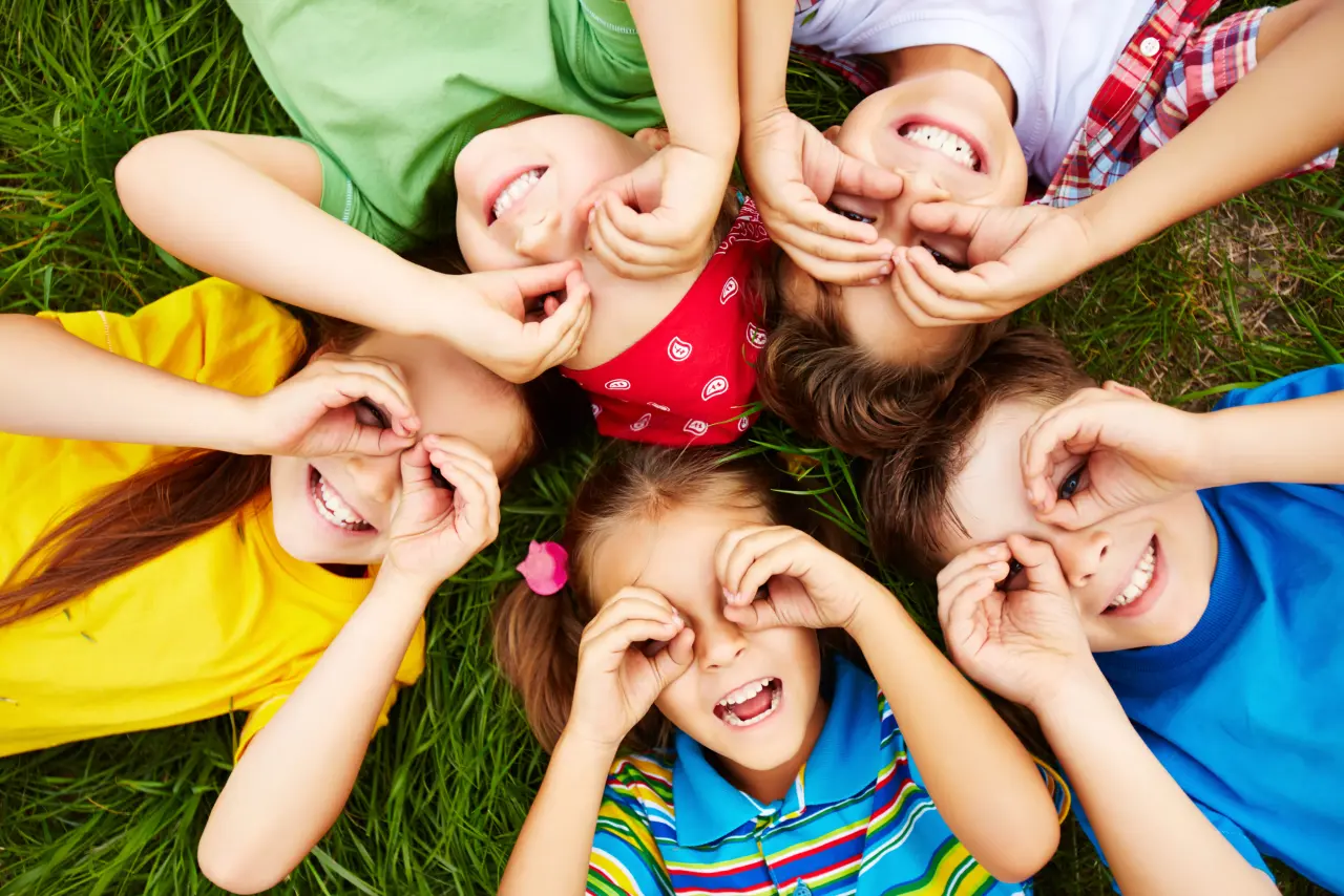 Children lying on grass, making pretend glasses with hands.