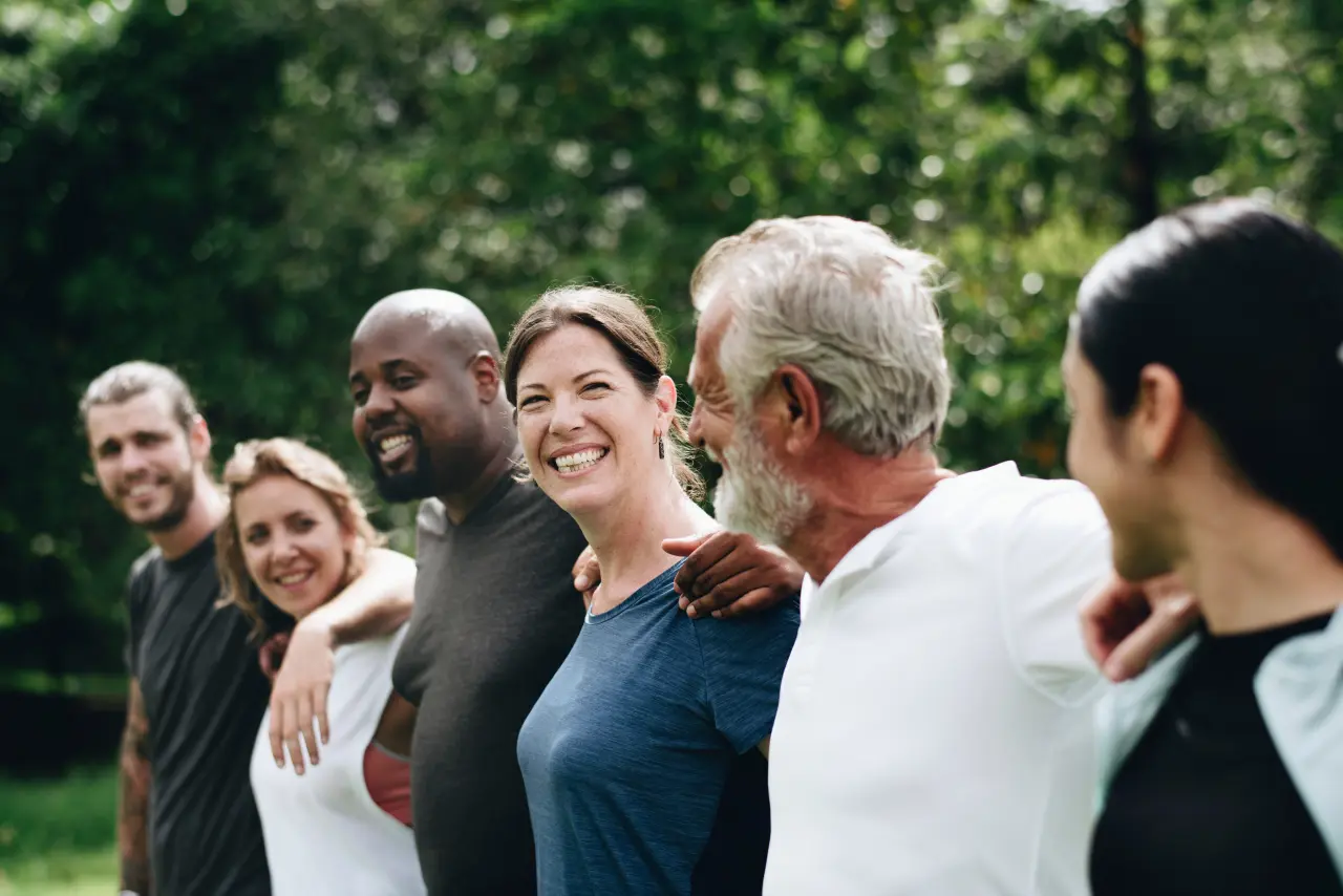 Group of diverse people standing arm in arm, smiling outdoors.