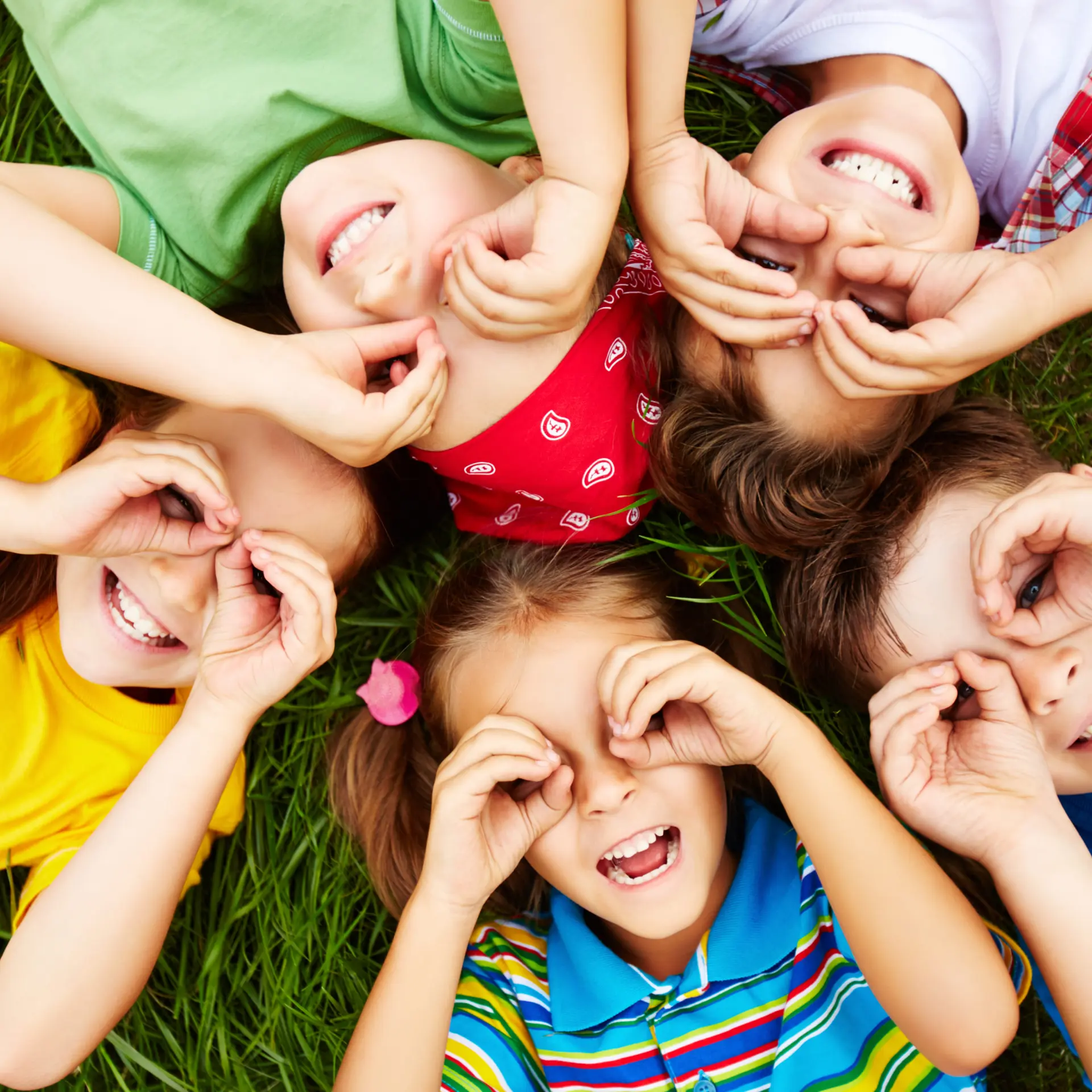 Children lying on grass, making pretend glasses with hands.