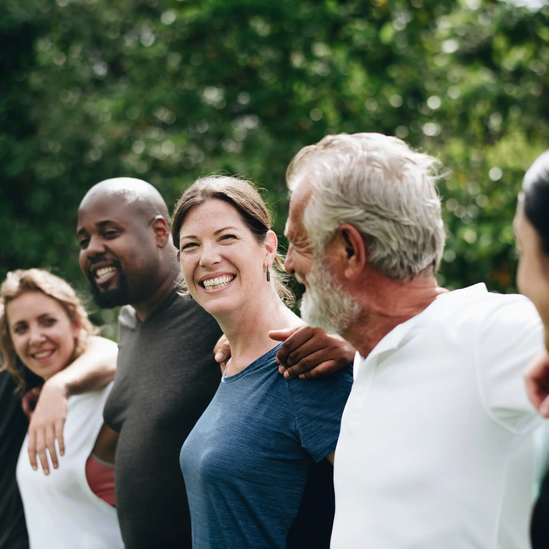 Group of diverse people standing arm in arm, smiling outdoors.