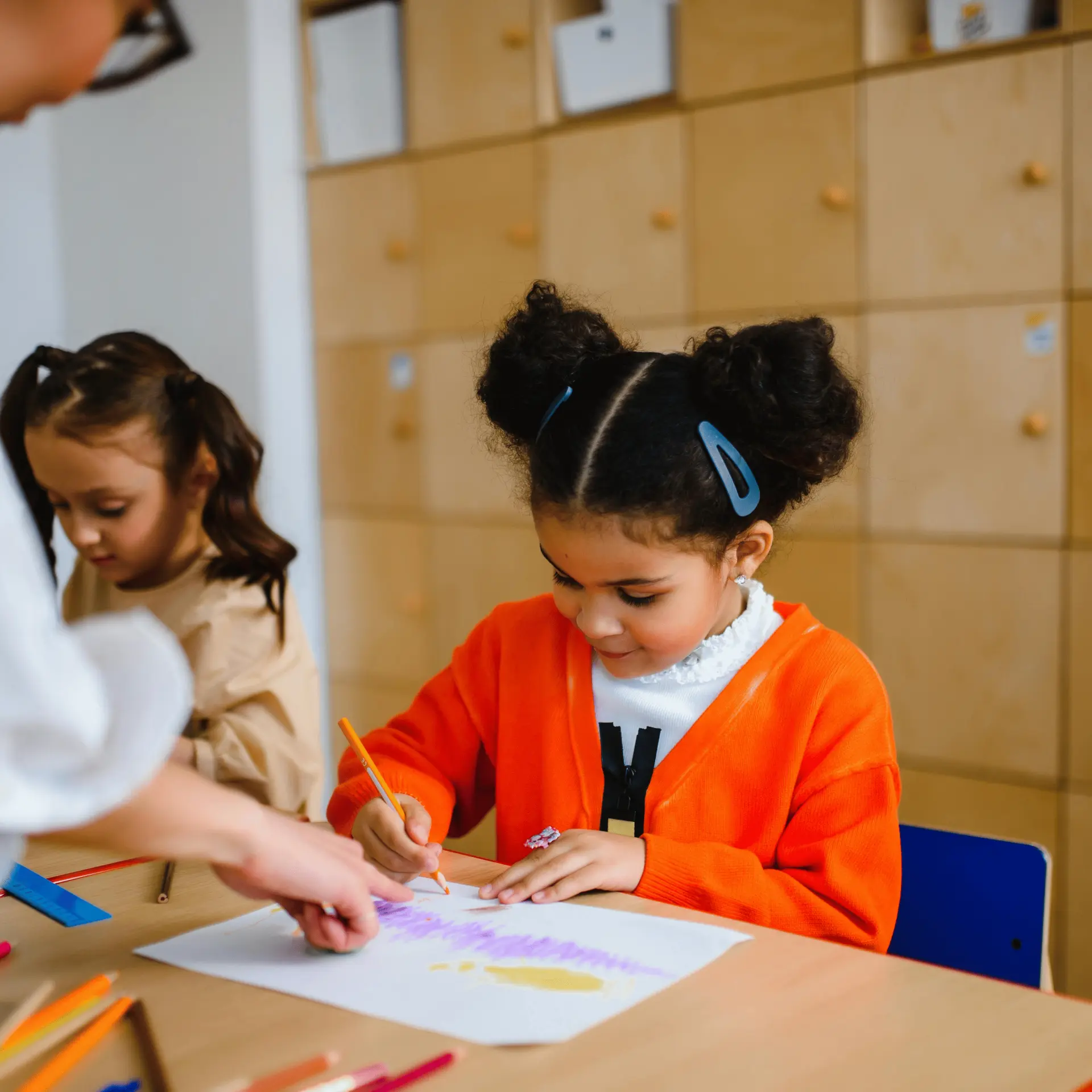 Children drawing with colored pencils at a table in a classroom.