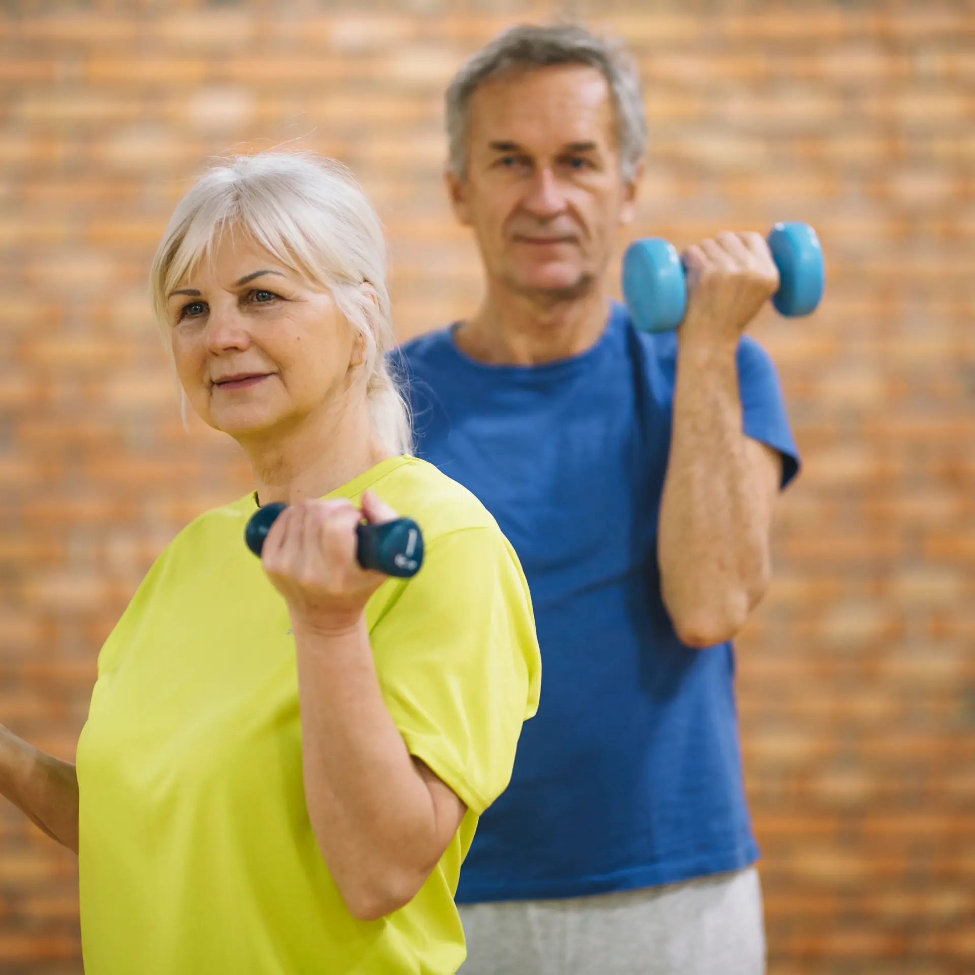 Older adults exercising with dumbbells, brick wall background.