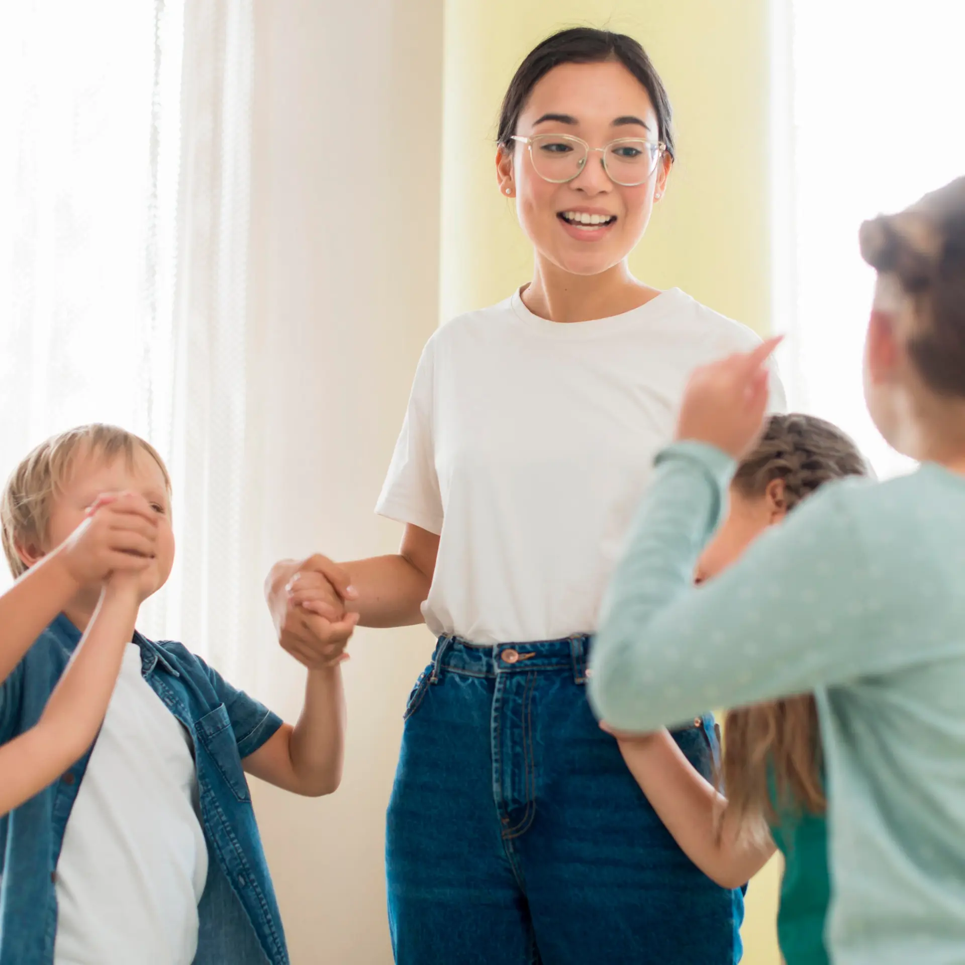 Adults and children holding hands indoors, smiling and engaged in activity.