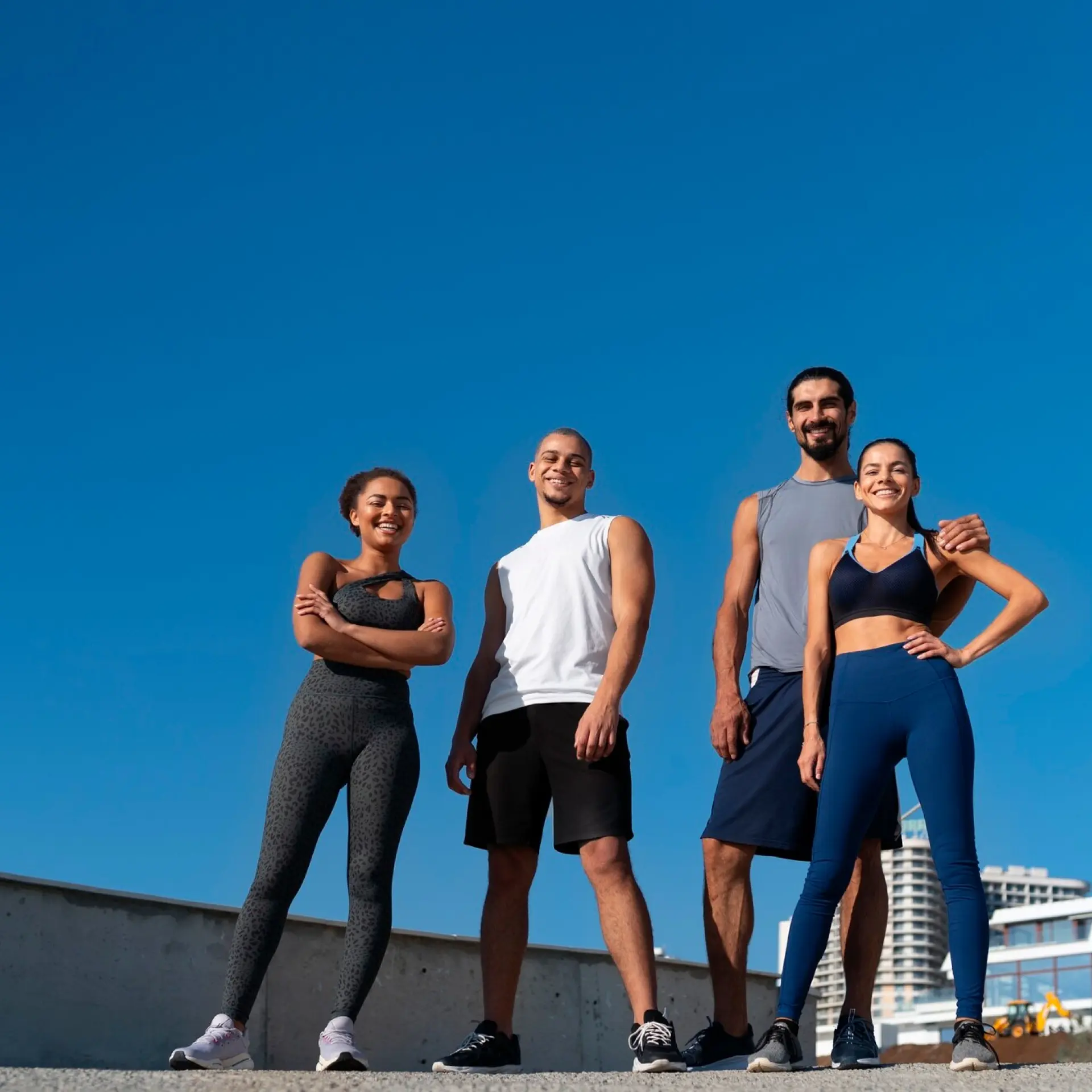 Four people in sportswear smiling outdoors under a clear blue sky.