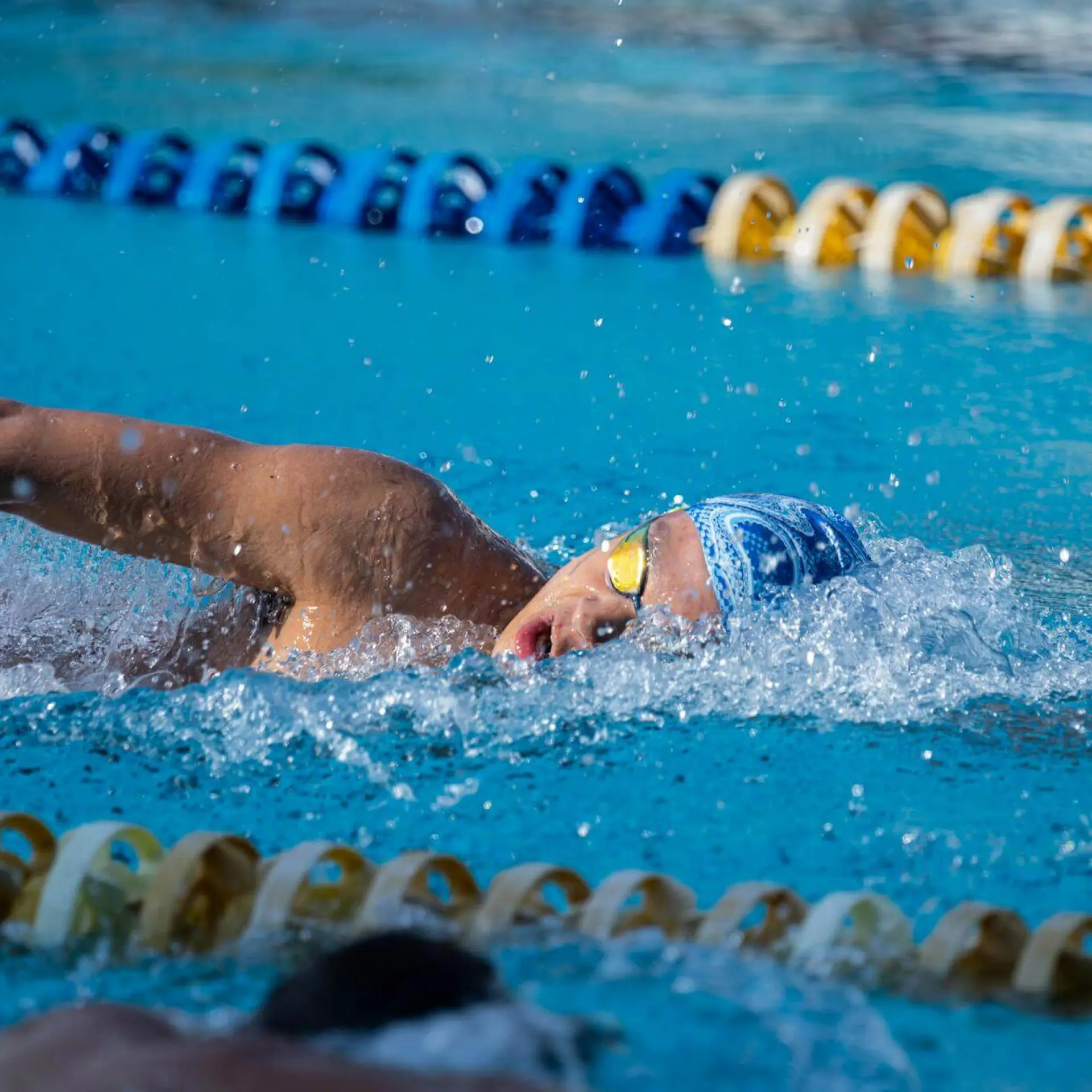 Swimmer in a pool, wearing goggles and a cap, mid-stroke near lane dividers.
