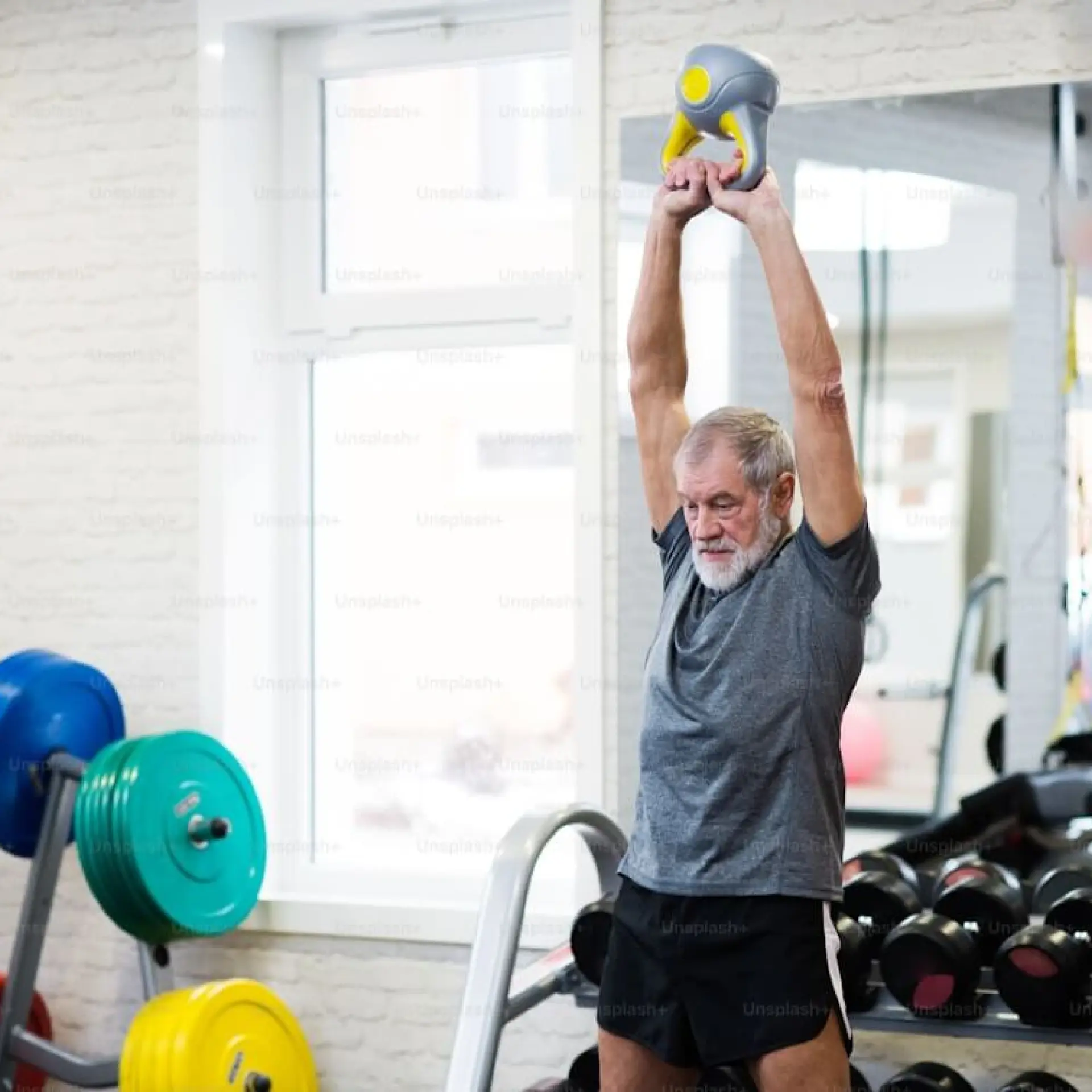 Man lifting a kettlebell in a gym, surrounded by weights and mirrors.