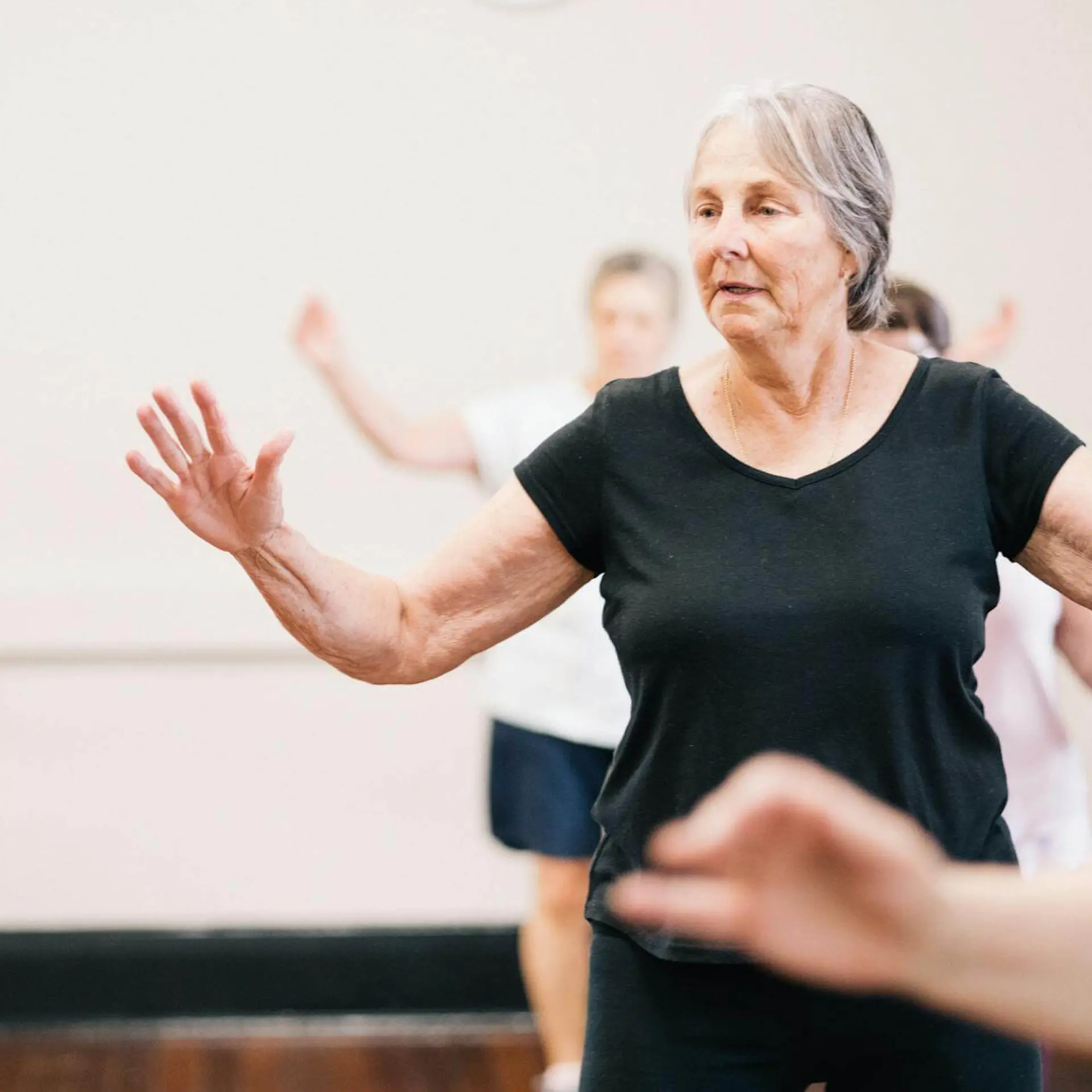 Elderly woman in exercise class, arms raised, focused expression.