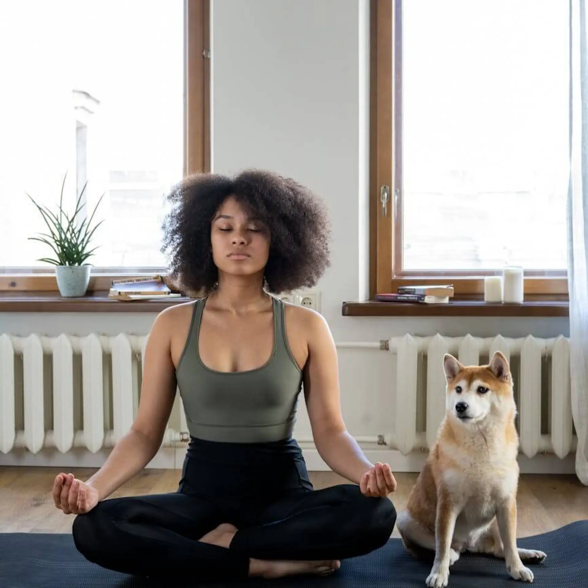 Woman meditating on yoga mat with dog beside her.